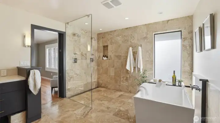 Spa-inspired bath features dual vanities, heated travertine floors, a generous soaking tub, a separate travertine shower, and a spacious walk-in closet.