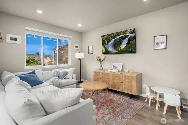 Living room area features warm colored engineered hardwood floors and large picture window that allows an abundance of natural light.  Built-in flat screen TV.