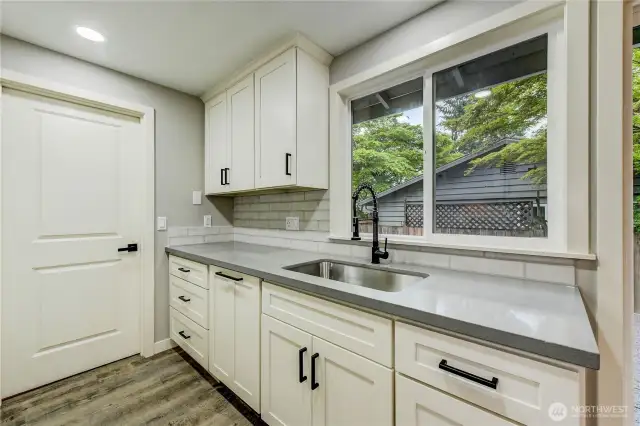 The deep stainless-steel sink with a matte black pull-down faucet sits beneath a sunny window, while the open layout flows seamlessly into the dining area and out to the backyard—ideal for both everyday living and entertaining.