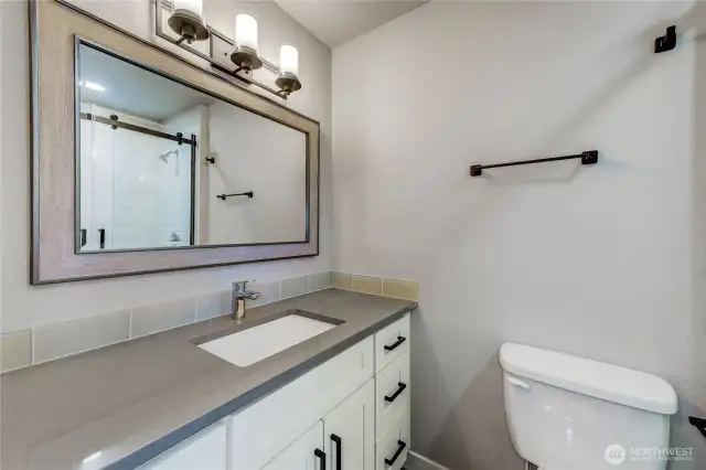 primary bathroom featuring a quartz-topped vanity with stylish black hardware, a framed mirror, and modern lighting.