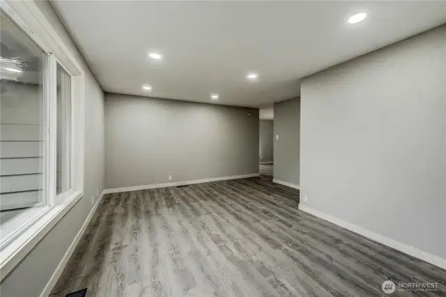 Spacious and versatile living area featuring wide-plank luxury vinyl flooring, recessed lighting, and large windows that invite in natural light.