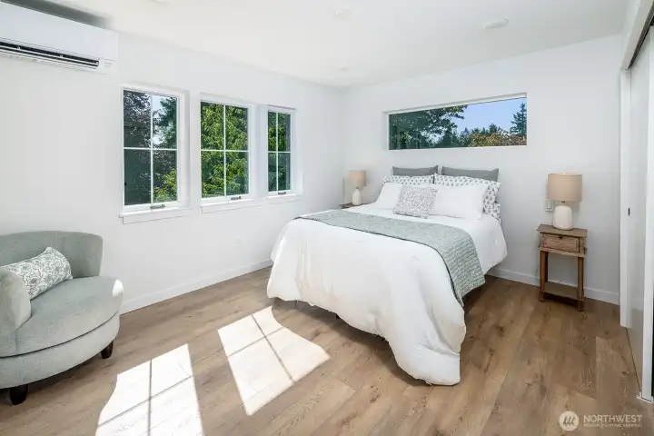 Primary bedroom with lush tree views from every window!  Natural wood grain design floors through this canopy suite.  Notice that the builder added two light switches on either side of the bed for easy control of detailed lighting.