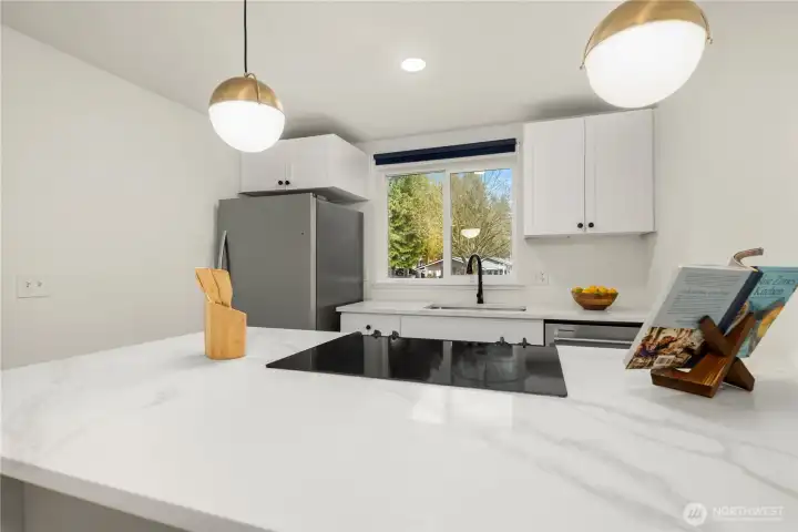 Kitchen with sleek quartz countertops and newer SS appliances. View from bar stool/Dining area on bright kitchen with plenty of daylight streaming in from the kitchen window. What a beautiful view for breakfast!