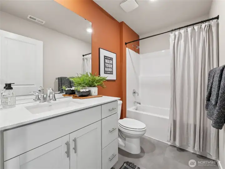 Stylish secondary bath pairs a quartz-top vanity and full tub/shower combo with a bold terracotta accent wall for designer flair. Pictures are for representational purposes only, colors and features may vary