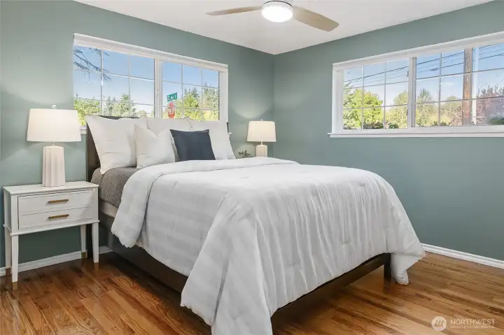 Primary bedroom with sunny corner windows and hardwood floors.