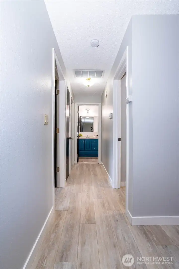 This interior hallway ties the bedroom wing of the home together, offering a clean, cohesive transition between private spaces. The luxury vinyl plank flooring runs continuously through the corridor, reinforcing the home’s updated feel while adding durability for everyday traffic. Neutral wall tones keep the space feeling bright and open rather than narrow, and the recessed lighting provides even illumination throughout. Multiple doorways branch off the hall, giving efficient access to bedrooms and bathrooms while maintaining separation from the main living areas. It’s a simple but important connective space that enhances the home’s functional layout — practical, low maintenance and visually consistent with the rest of the interior finishes.