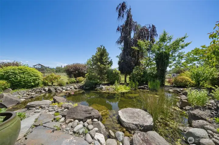 Pond with waterfall and professional landscaping with English garden feel. Plethora of rose bushes and orchard to the right.
