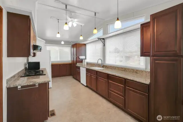Beautiful cherry toned kitchen cabinets with slab granite counters, ceiling  fan.
