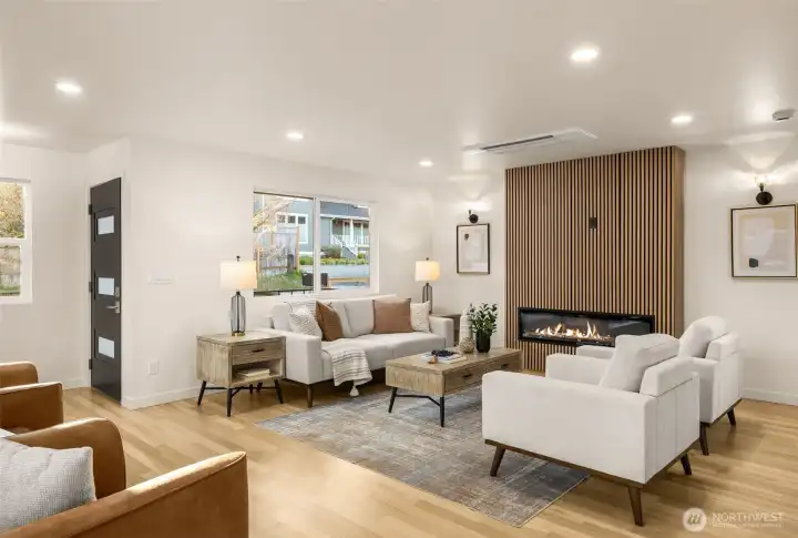 Spacious open-concept living area featuring a cozy wood slatted fireplace and large windows for a bright, airy feel