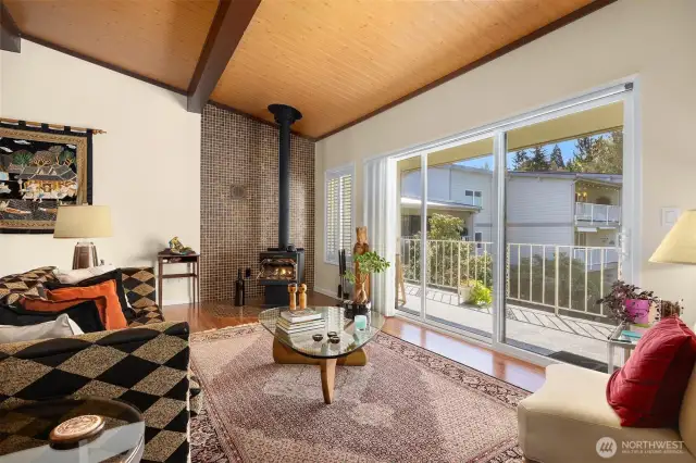 Spacious living room highlighted by a standalone wood-burning fireplacde, expansive windows, and a sliding glass door that fills the space with natural light. =