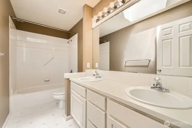Dual sinks, tile bath surround and white cabinets are featured in this large full bath on the upper floor.
