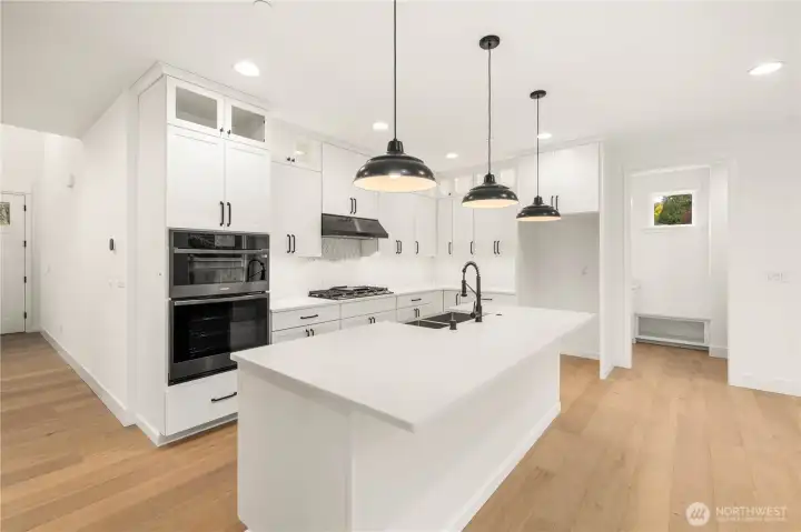 The kitchen features bright quartz countertops, a large island with undermount sink, and a full-height tile backsplash that elevates the clean, modern design. Black hardware and pendant lighting add contrast, while the spacious layout flows seamlessly into the main living areas for effortless entertaining and everyday convenience. The walk-in pantry and extensive cabinet storage create a truly functional Eastside-living hub.    These photos are from lot 3 at Gooden Hollow, the actual home for sale. However, other homes may vary, so all photos, renderings, site maps, and floorplans are for visualization purposes only. Plans, colors, building orientation, finishes, home outlook, and other details can and WILL vary.