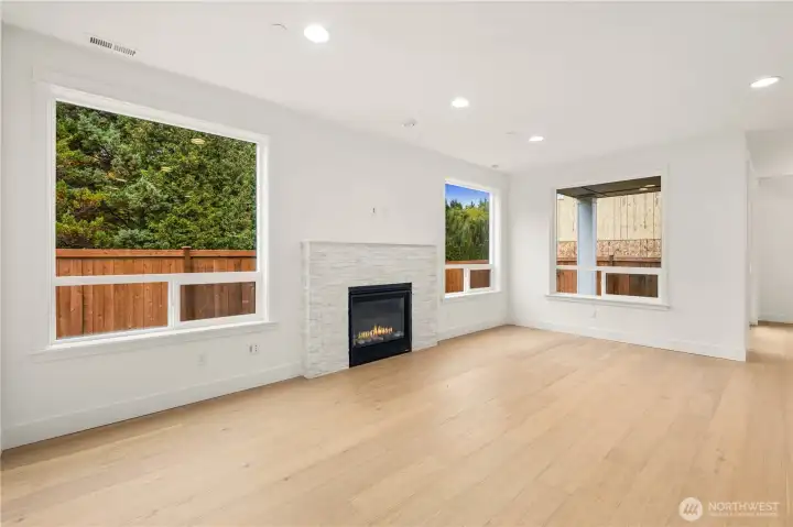 This bright main-level living area features wide plank engineered hardwoods, large picture windows framing the private fenced yard, and a sleek gas fireplace with a modern stacked-stone surround. The open layout creates a seamless flow into the kitchen and dining spaces, perfect for relaxed Eastside living and effortless entertaining.    These photos are from lot 3 at Gooden Hollow, the actual home for sale. However, other homes may vary, so all photos, renderings, site maps, and floorplans are for visualization purposes only. Plans, colors, building orientation, finishes, home outlook, and other details can and WILL vary.
