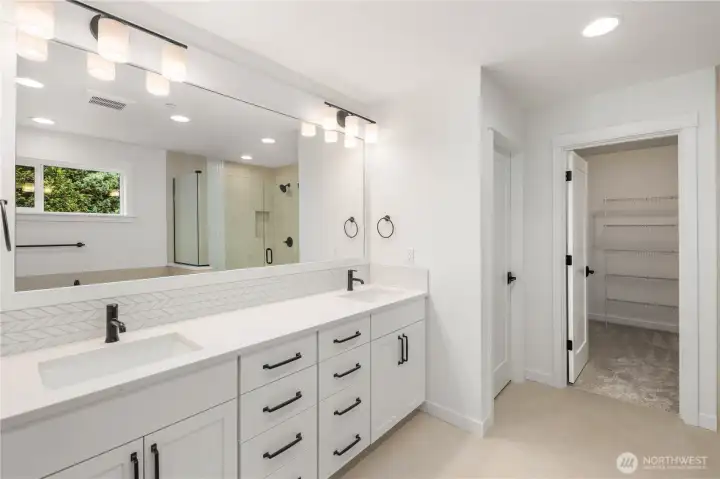 This spacious ensuite bath features an extended double vanity with quartz countertops, black fixtures, and abundant drawer storage. Soft lighting and a full-width mirror create a bright, calm start-to-finish routine, with direct access to the walk-in closet for everyday convenience.    These photos are from lot 3 at Gooden Hollow, the actual home for sale. However, other homes may vary, so all photos, renderings, site maps, and floorplans are for visualization purposes only. Plans, colors, building orientation, finishes, home outlook, and other details can and WILL vary.