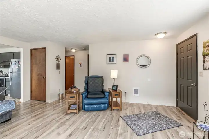 Spacious living room featuring fresh paint, new flooring, and updated light fixtures. View looks toward the hallway leading to the full bathroom and two bedrooms.