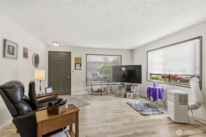 View of the spacious living room looking toward the front entryway, highlighting the bright, open layout and updated flooring.
