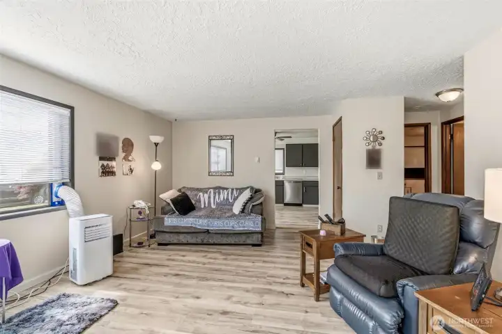 Open-concept layout showcasing the spacious living room with the updated kitchen in the background and a hallway leading to the bedrooms and full bath.