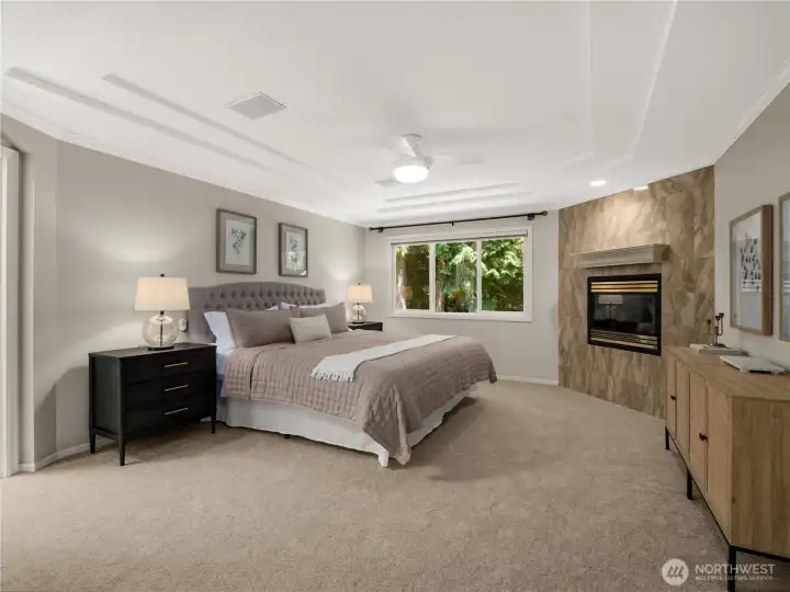End each day in the comfort of this spacious primary suite, where a cozy fireplace, soaring tray ceiling, and picturesque window overlooking lush greenery create a calming, spa-like ambiance. End each day in the comfort of this spacious primary suite, where a cozy fireplace, soaring tray ceiling, and picturesque window overlooking lush greenery create a calming, spa-like ambiance.
