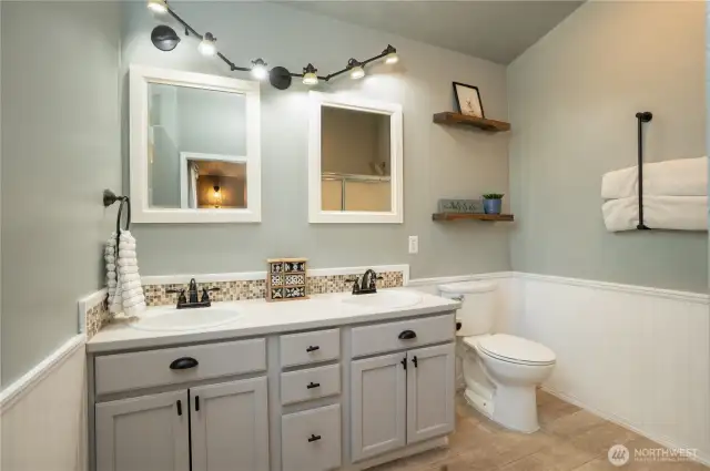 Primary bathroom with double sink vanity, tile plank flooring, wainscotting, and tile backsplash.