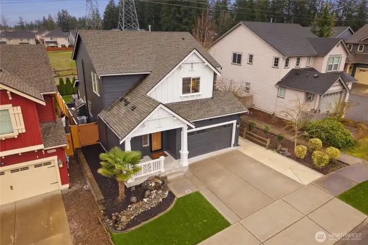 Aerial view of the home’s front exterior showcasing the welcoming covered entry, attached garage, and cleanly maintained front yard. The perspective highlights the home’s curb appeal and its placement within the surrounding neighborhood.