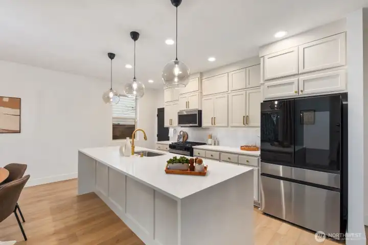 Expansive kitchen island with integrated sink and statement pendant lighting creates a natural gathering space for cooking, conversation, and casual seating. The kitchen layout opens directly to the dining area, supporting an easy flow for entertaining.