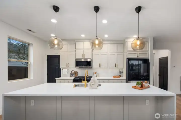 Clean-lined kitchen design centered around a large island and full wall of cabinetry, offering abundant storage and prep space. Pendant lighting and recessed ceiling lights keep the kitchen bright and welcoming throughout the day.