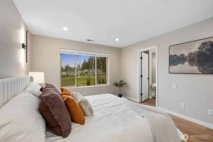 From this angle, the primary suite highlights its airy proportions and calming neutral palette. Large windows bring in natural light and neighborhood views, enhancing the serene atmosphere of this private bedroom retreat.