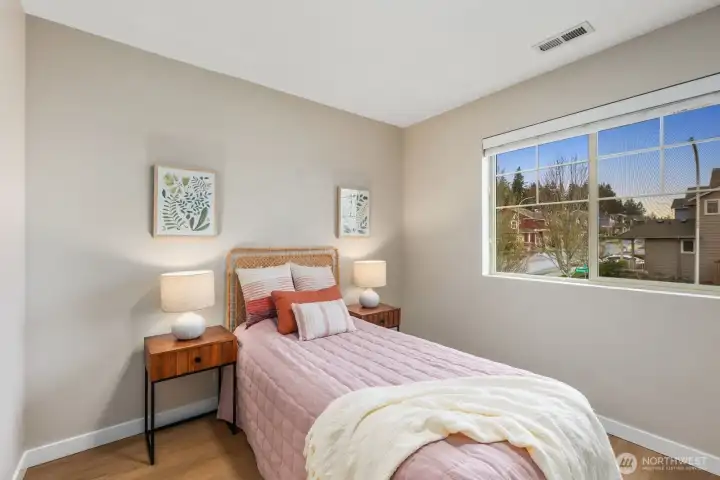 Light-filled bedroom with large window bringing in neighborhood views and natural daylight. A comfortable layout with space for bedside tables creates a calm and functional retreat within the home.