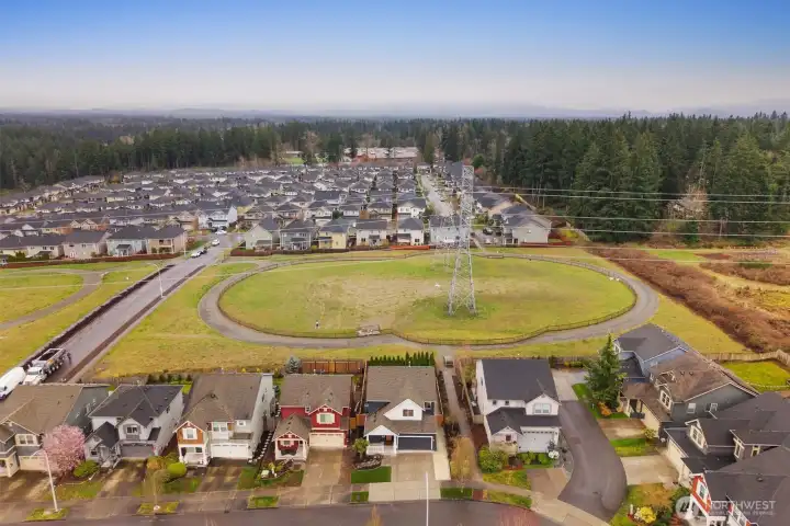Wide aerial view of the surrounding neighborhood featuring nearby open green space and walking paths. The perspective highlights the home’s location within a well-established residential community.