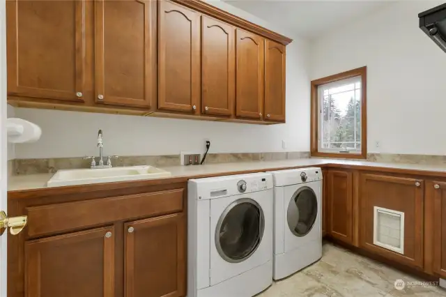 Oversized laundry room with Built in Cabinets galore, Utility Sink, Under Counter Washer and Gas Dryer, Laminate Countertop and 13”x13” Tile Flooring.