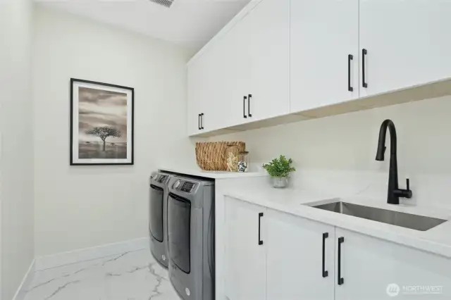 Laundry room comes equipped with laundry machines and custom cabinetry