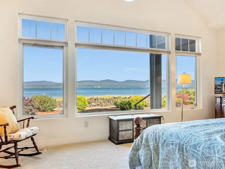 Expansive windows fill the primary suite with natural light while showcasing stunning waterfront scenery.