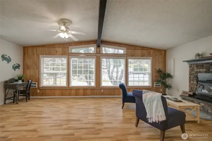 Very large living room with wall-to-wall windows, vaulted ceiling, wood beam, ceiling fan and laminate flooring