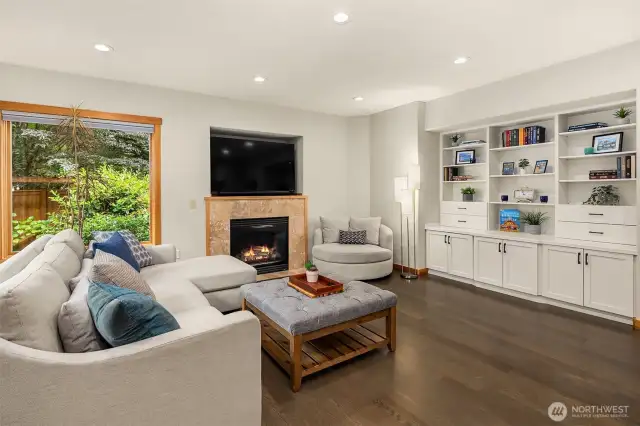 White Oak hardwood floors flow throughout the main level into a spacious family room with one of two fireplaces with travertine tile surround, built-in bookcases, cabinets and views to the outdoor space.