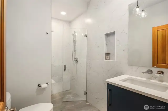 A beautifully remodeled 3/4 bath on the main level ~ a curb-less shower with frameless glass door, floating vanity, high-end fixtures, lighting, and stunning floor-to-ceiling tilework.