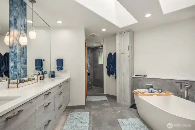 A lavish, stunning, 5-piece en suite bath boasting heated floors, soaking tub, floating dual vanity, large pass-through shower with rain head, bench, and beautiful tilework, fixtures & lighting.