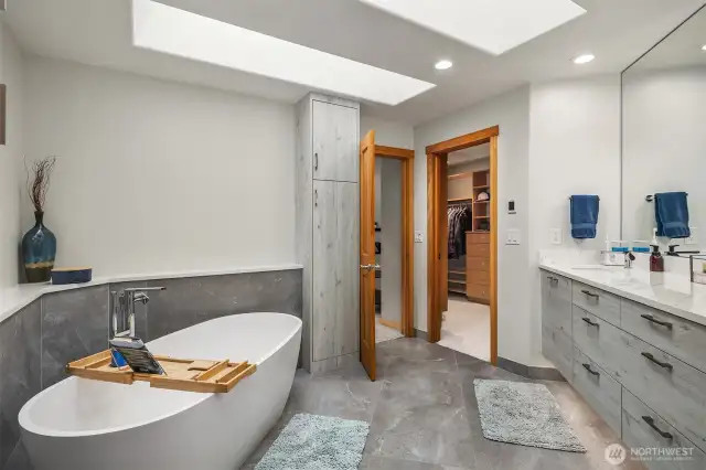 A lavish, stunning, 5-piece en suite bath boasting heated floors, soaking tub, floating dual vanity, large pass-through shower with rain head, bench, and beautiful tilework, fixtures & lighting.