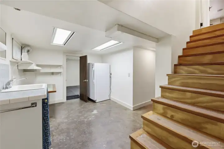 entrance to the basement, utility sink and freezer. Room beyond is set up for an exercise room and has a storage closet.