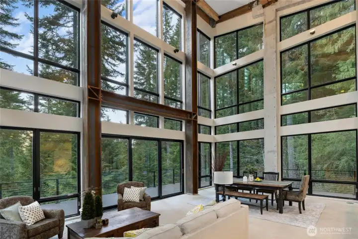 A view of the living room and dining room. The custom steal beams with floor to ceiling windows gives the home such a great vibe. You almost feel like you are in a very elegant tree house!