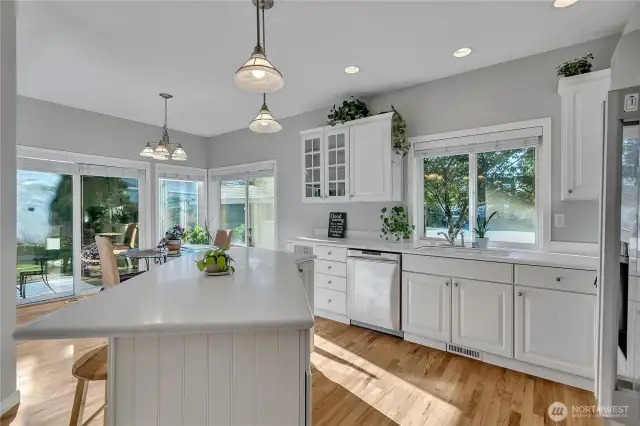 A view of the kitchen, featuring Corian countertops, extensive cabinets and an island (with overhead spot lighting), and hardwood flooring. New appliances will remain.