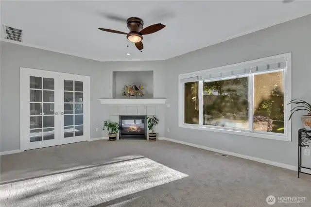 The family room, with its gas fireplace and a wall niche. The room also has a ceiling fan incorporating an overhead light. French doors lead to an office. There are large windows overlooking the backyard's continuously flowing fishpond.