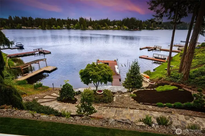 The terraced rock and riverstone landscaping creates texture and dimension without cluttering the sightlines, so your lake views stay wonderfully open instead of disappearing behind overgrown shrubs every summer. The low-profile plantings soften everything naturally while still keeping maintenance manageable, and the flagstone pathway leading down toward the lower patio and bulkhead feels substantial, polished and incredibly inviting. The lawn stays lush with front and back sprinkler systems already on timers, which means less time dragging hoses around and more time actually enjoying the property. And the setting on the lake itself is especially appealing too. This section of Long Lake has a quieter cove-like feel because it sits slightly tucked away from the faster straightaway boating traffic, giving you a more peaceful waterfront experience while still fully enjoying all the recreation the lake offers.