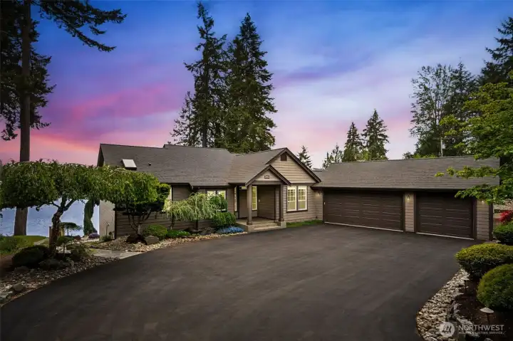 The extra-wide driveway creates such an easy arrival experience for guests while also making everyday life dramatically more convenient, especially at a waterfront property where coolers, paddleboards, groceries and random lake gear always seem to multiply. The driveway flows directly to both the covered front porch and the flagstone path leading toward the water, making loading and unloading feel effortless instead of turning into an accidental CrossFit workout. The three-car garage setup is fantastic too, with an 18’ wide double door plus a separate 9’ single bay, both with impressive 8’ height clearance ready for taller trucks and SUVs. Inside, the garage includes extensive storage racks that stay with the home along with a utility sink for cleanup convenience. Framing everything outside are mature low-maintenance plantings and river rock landscaping that keep the property looking beautifully established without demanding endless upkeep every weekend.