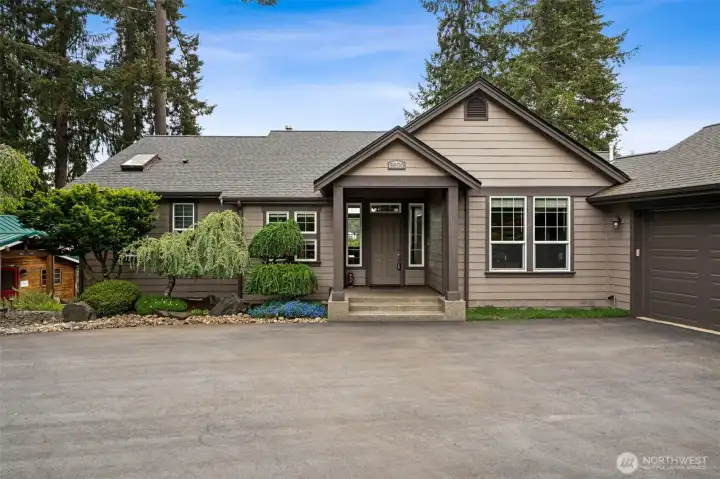 This front entry feels welcoming before you even reach the door. The approach is wonderfully easy with just three low-profile steps leading up to the covered porch, making everyday access feel comfortable and approachable while still maintaining that stately custom-home presence. And the architectural details continue impressing even on the non-waterfront side of the house. The windows are beautifully designed with divided-light detailing between the panes plus operable lower sections that allow fresh airflow without disrupting the clean visual lines of the home. Thoughtful details like that make such a difference over time. The roof also deserves a little appreciation because it was replaced in 2017, giving buyers the peace of mind of knowing one of the home’s biggest systems already has plenty of life left ahead. The covered porch feels substantial and welcoming with its wood-paneled ceiling, aggregate concrete and stately architectural lines that immediately give custom home vibes.