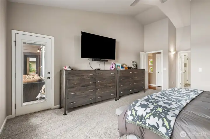 At approximately 15x23, the primary suite bedroom easily accommodates large furniture pieces without ever feeling crowded, and seeing those two substantial dressers in place really helps show the scale here. The vaulted ceilings continue through the space, adding even more openness, while the glass door leading directly out to the deck creates such a beautiful connection to the water. Morning coffee with lake views without even leaving your bedroom? Yes please! The layout is smart too. The en suite bath sits privately off to the side, while the hall closet directly across from the bedroom adds even more practical storage complete with interior lighting.