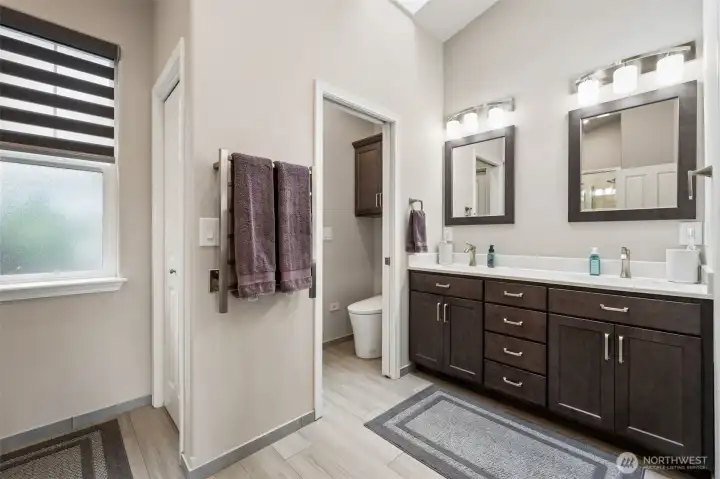 Newly remodeled and beautifully thought out, the space layers practical luxury everywhere you look, starting with the heated tile floors that make cold mornings dramatically less offensive. Then there is the heated towel rack, dimmable lighting and skylight overhead bringing in soft natural light during the day while still keeping the room wonderfully private thanks to the frosted window glass. The long dual-sink vanity gives each person their own dedicated space and mirror, which frankly should be mandatory in every relationship. The charcoal cabinetry adds rich contrast against the lighter finishes and comes loaded with pull-outs and soft-close hardware so the storage actually functions beautifully. There is even a separate toilet room complete with a bidet. The walk-in closet w/built-ins create designated space for shoes, accessories, hanging clothes & all the other wardrobe pieces that usually end up stacked awkwardly on a chair somewhere after three busy days.