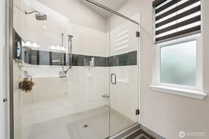 This oversized walk-in shower is beautifully done with a mix of cultured marble and tile finishes wrapped behind sleek glass doors that keep the entire room feeling open and polished. The scale here is fantastic too. This is not one of those showers where you spend half your morning elbowing the wall every time you turn around. With dual showerheads and all that space, it feels much more like a private spa setup than a standard residential bathroom, and the newer tankless water heater offers endless hot water to this home too!