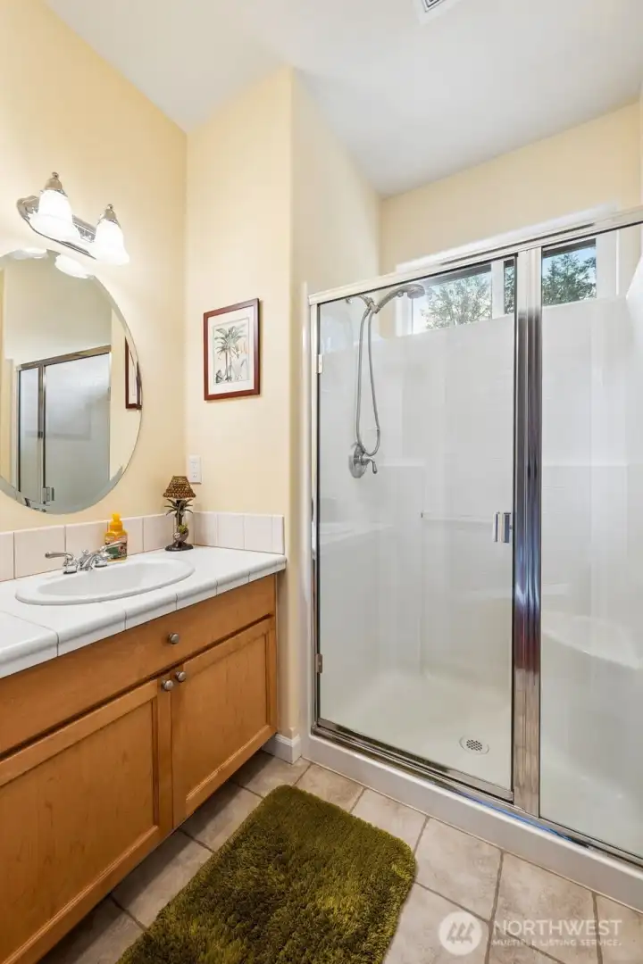 Located on the main floor beside the den, this three-quarter bath creates an incredibly flexible guest setup thanks to the den’s second hallway entrance connecting directly nearby. Overnight guests basically get their own tucked-away little suite arrangement without needing to trek through the house in pajamas carrying a toothbrush. The location near the garage entry is another underrated win too, especially for lake life where sandy feet, wet swimsuits and outdoor projects are simply part of the lifestyle. The room itself feels warm and cheerful with soft buttercream walls, tile flooring and maple cabinetry coordinating beautifully with the kitchen. The oversized shower with glass doors includes a molded seat and operable window above for airflow, while the tiled vanity and beveled round mirror keep the whole space feeling polished and welcoming.