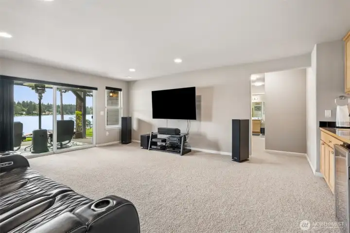 At roughly 16x22, the lower level family room bonus space easily handles big gatherings, movie nights, rainy-day game tournaments or the inevitable crowd that migrates downstairs after dinner because somebody opened the slider and everybody followed the lake view. And yes, the views continue down here too. That massive sliding glass door keeps Long Lake front and center while giving direct access to the hot tub, dock path and waterfront beyond. The layout is incredibly smart as well. Bedrooms are split to opposite sides of the lower level for added privacy, making the downstairs setup ideal for guests, teenagers, multigenerational living or simply giving everyone a little breathing room. Recessed lighting keeps the room bright without visual clutter, soft carpeting adds comfort underfoot and tucked off to the side sits the beverage bar because clearly this house understands hospitality.