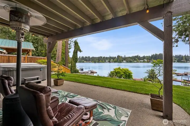 Tucked beneath the upper deck, the space offers cool shade while still soaking in those spectacular Long Lake views stretching across all 57 feet of waterfront. And then there is the hot tub, only four years old and included with the home, sitting there practically begging for late-night lakefront soaking sessions after a long day on the water. From this angle you really start appreciating how beautifully the property connects to the shoreline, with easy access down toward the dock and waterfront while still feeling private and relaxed back near the house.